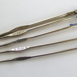 May include: Five silver crochet hooks of different sizes. The hooks are labeled with their sizes: "Clover 15/0", "Made in USA", "Size 14/0", "Clover 2", and "Clover 1".