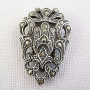 Puede incluir: Un broche de plata y marcasita con un dise&ntilde;o delicado y ornamentado. El broche tiene forma de l&aacute;grima y presenta un motivo floral.
