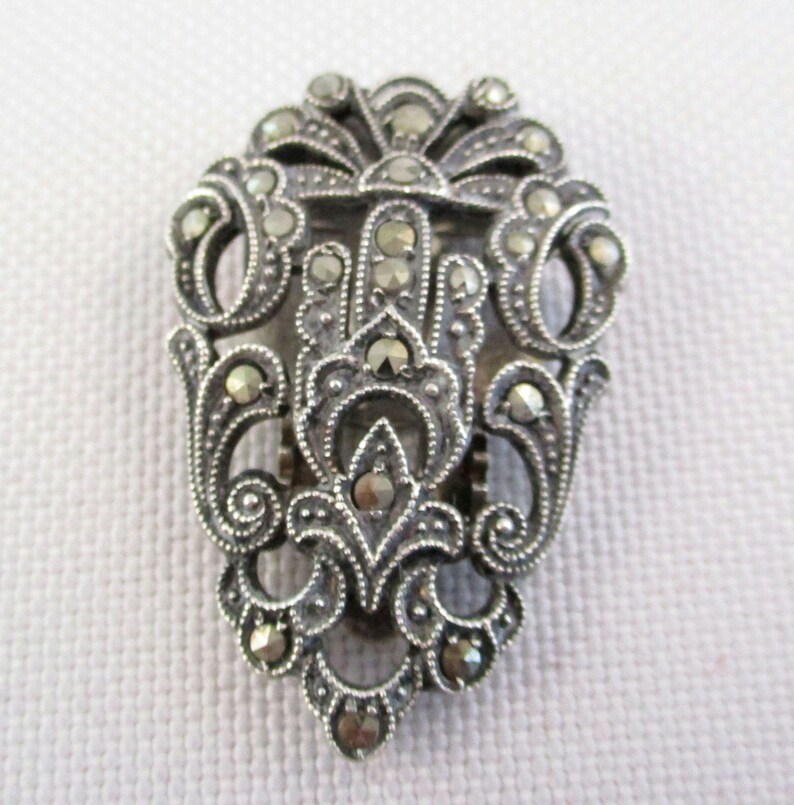 Puede incluir: Un broche de plata y marcasita con un dise&ntilde;o delicado y ornamentado. El broche tiene forma de l&aacute;grima y presenta un motivo floral.