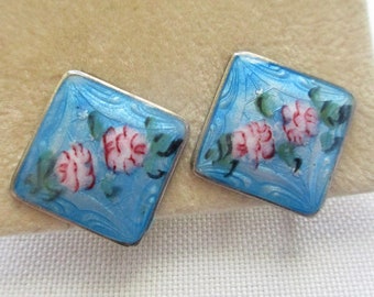 May include: A pair of blue enamel earrings with a floral design. The earrings are square shaped and have a silver setting.