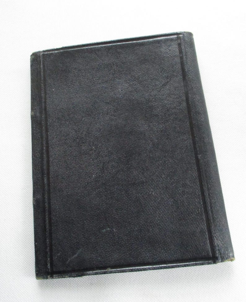 May include: A small, rectangular, black book with a textured cover. The book has a simple, classic design with a dark, solid colour. The edges of the book are slightly worn, suggesting age or use.