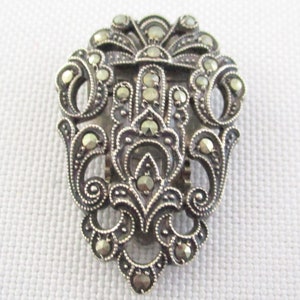 Puede incluir: Un broche de tono plateado con un dise&ntilde;o floral detallado, engastado con piedras de marcasita.