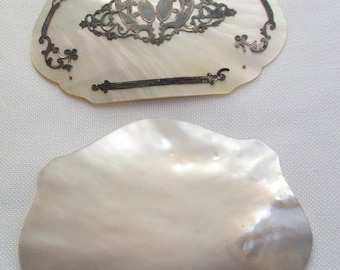 May include: Two antique mother of pearl shell pieces with silver filigree designs. The top piece has a silver filigree design in the center and a silver band across the bottom. The bottom piece is plain.