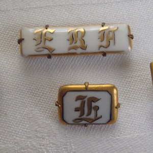 May include: Four white porcelain buttons with gold trim and black lettering. The buttons feature the letters "F", "R", and "H" in a stylized font.