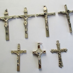 May include: A collection of seven silver-toned crucifix pendants. Each cross features a detailed depiction of Jesus Christ. The crosses vary in design, with some having a simple, rectangular shape and others with ornate detailing.