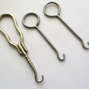 May include: Three silver shoe horn tools. One has a loop handle and a hook on the end. The other two have a circular handle and a hook on the end.