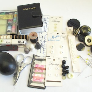May include: A vintage sewing kit with a black leather case, a variety of needles, thread, buttons, and other sewing supplies. The kit also includes a small pair of scissors, a thimble, and a bobbin.