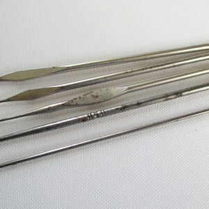 May include: A set of six silver crochet hooks of varying sizes. The hooks are arranged in a row, with the largest hook at the top and the smallest hook at the bottom.