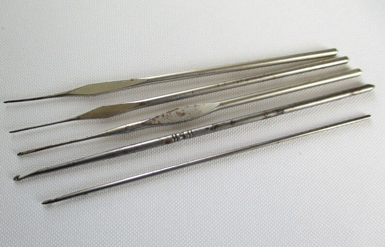 May include: A set of six silver crochet hooks of varying sizes. The hooks are arranged in a row, with the largest hook at the top and the smallest hook at the bottom.