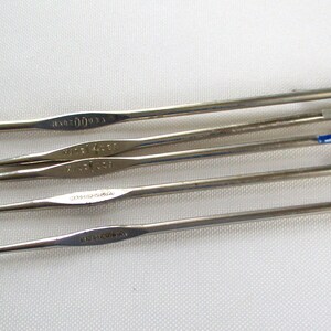 May include: A set of six silver crochet hooks of varying sizes. The hooks are arranged in a row, with the largest hook at the top and the smallest hook at the bottom.
