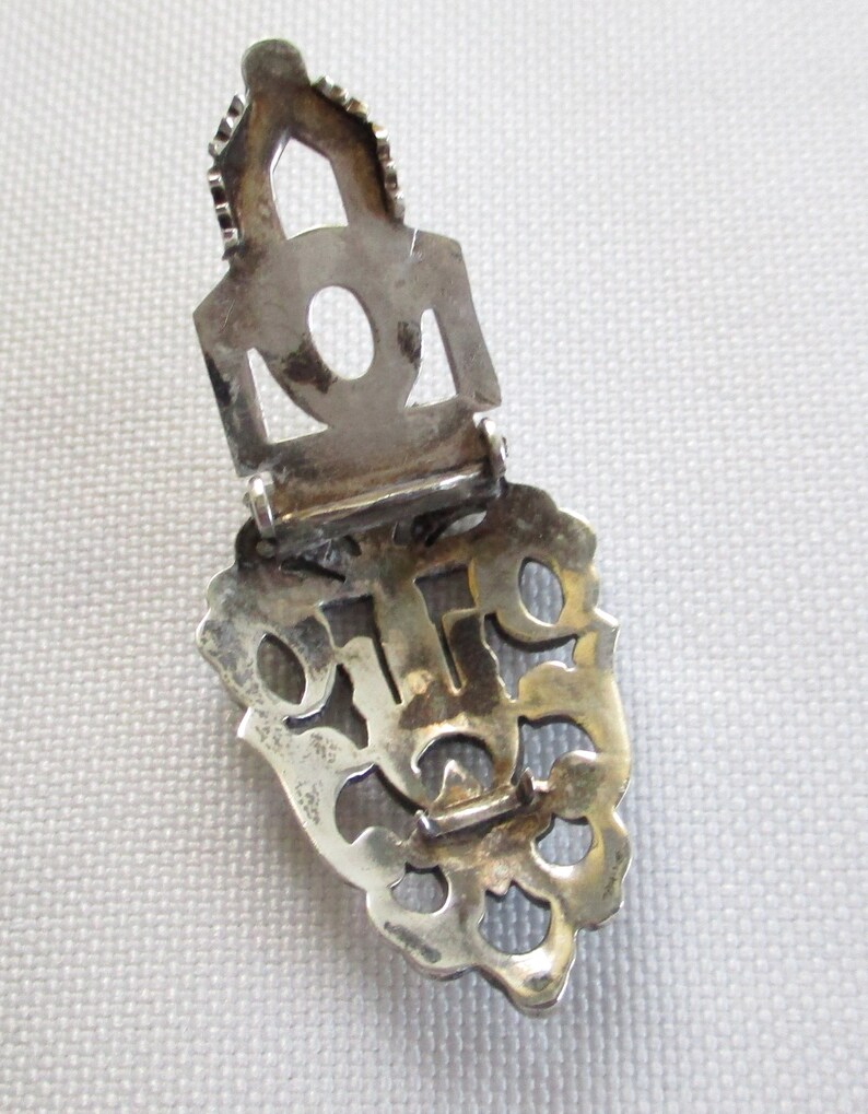 Puede incluir: Cierre de filigrana de plata con un dise&ntilde;o decorativo. El cierre est&aacute; abierto y la parte posterior es visible. El cierre est&aacute; hecho de plata y tiene un acabado brillante.