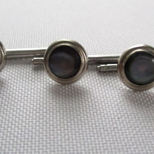 May include: A set of four silver shirt studs with black pearl-like centers.