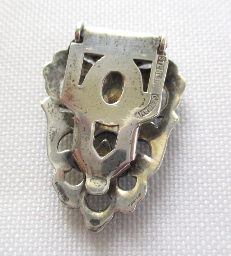Puede incluir: Un broche de filigrana de plata con un cierre en la parte posterior. La parte posterior del broche est&aacute; marcada con "STERLING GERMANY".