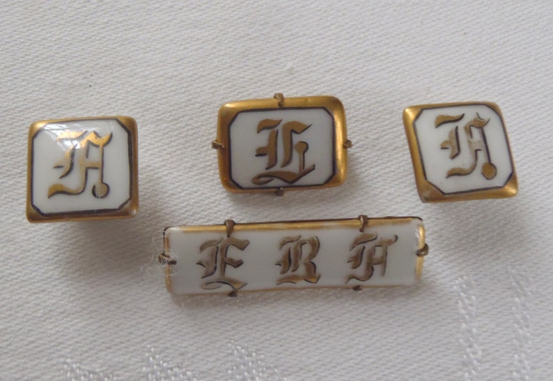 May include: Four gold-toned porcelain buttons with white enamel and gold lettering. The buttons feature the letters "F", "R", and "H" in a stylized font.