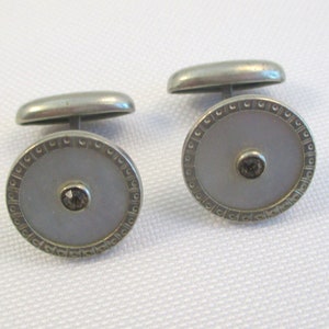 May include: A pair of silver cufflinks with a white mother of pearl center and a clear rhinestone in the center of each cufflink.