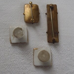 May include: Four vintage porcelain brooches with gold trim. The brooches have a white background and a gold pin on the back.