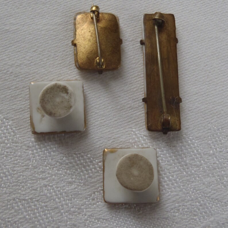 May include: Four vintage porcelain brooches with gold trim. The brooches have a white background and a gold pin on the back.