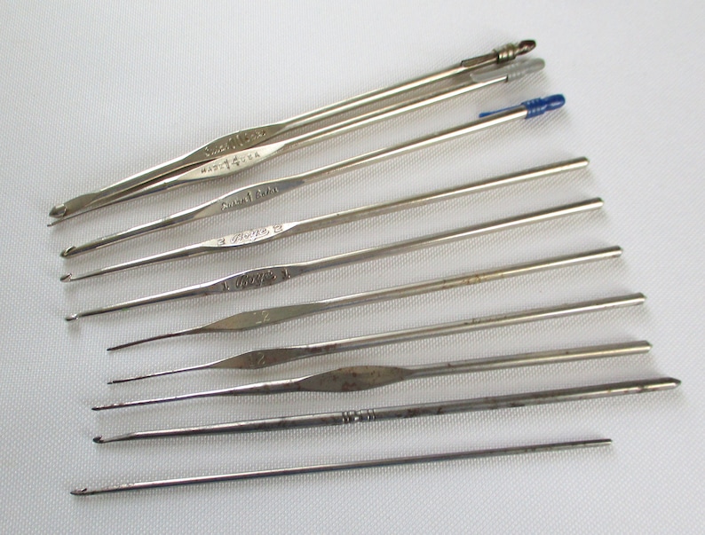 May include: A set of ten silver crochet hooks of varying sizes. The hooks are arranged in a row from largest to smallest. The hooks are labeled with their size in millimeters.