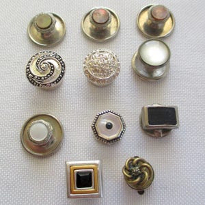 May include: A collection of 10 silver and gold cufflinks with various designs, including a swirl, a geometric pattern, a black square, and a white circle.