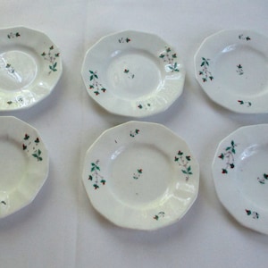 May include: Set of six white ceramic plates with a scalloped edge and a green and red floral design.