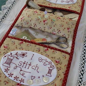May include: A beige fabric sewing kit with red trim and white embroidered patches. The patches say "I stitch" and "Himb!" The kit has pockets for needles, thread, and scissors.