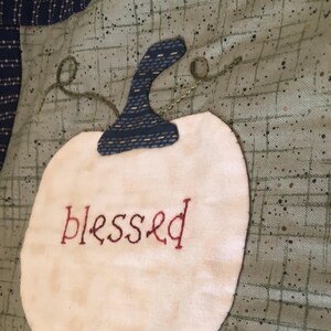 May include: A white fabric pumpkin with a blue fabric stem and the word "blessed" embroidered in red thread.