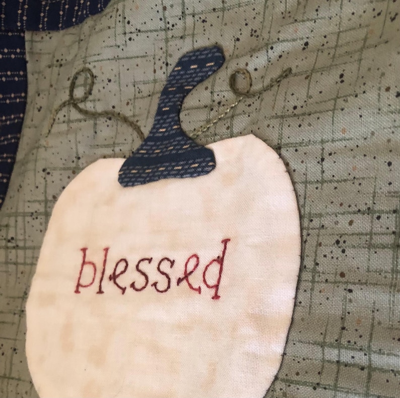 May include: A white fabric pumpkin with a blue fabric stem and the word "blessed" embroidered in red thread.