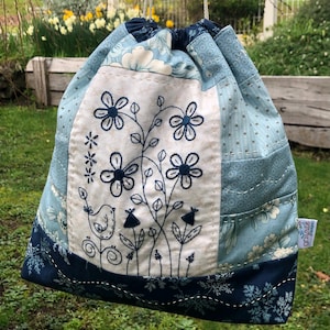 May include: A blue and white drawstring bag with a floral embroidery design. The bag is made of patchwork fabric and has a blue and white floral print on the bottom.