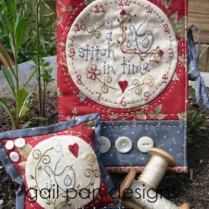 以下が含まれることがあります： 赤い白の布製の針刺しで、青い鳥と「a stitch in time」という文字が時計の文字盤に刺繍されています。針刺しには、青い鳥とハートが白い円に刺繍された、より小さな赤い白の布製の針刺しが付いています。布には「gail pan designs」と「a stitch in time」の文字が印刷されています。白い糸の糸巻きも含まれています。