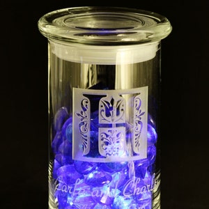 May include: A clear glass jar with a lid, filled with blue and purple glass gems. The jar is engraved with the letters "T & C" and the text "Tara and Charles April 30, 2016".