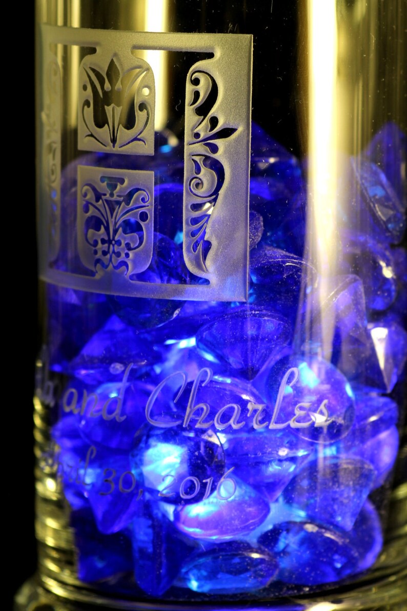 May include: A clear glass with blue glass beads inside. The glass is etched with the text "Lisa and Charles" and the date "Jul 30, 2016".