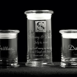 May include: Three clear glass jars with lids, each engraved with a name. The center jar has the names "Brittany & David" and the date "July 2, 2016". The left jar has the name "Brittany" and the right jar has the name "David".