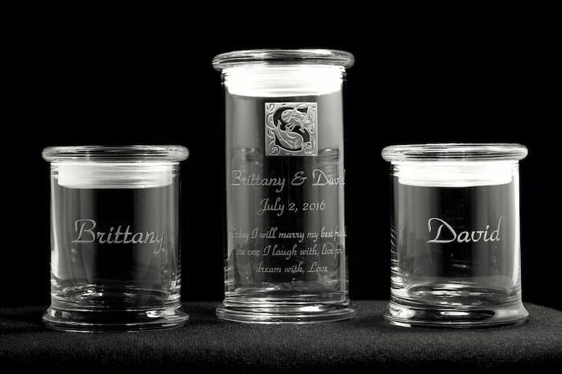 May include: Three clear glass jars with lids, each engraved with a name. The center jar has the names "Brittany & David" and the date "July 2, 2016". The left jar has the name "Brittany" and the right jar has the name "David".