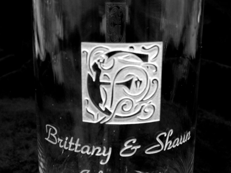 May include: A clear glass with a decorative etched design of a letter "B" with swirls and the text "Brittany & Shawn" below.