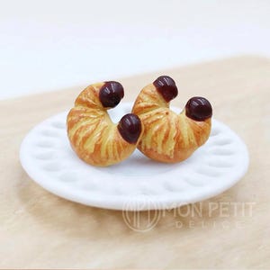 Golden handmade miniature croissant stud earrings in polymer clay, front view