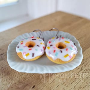 Angled view of the white donut earrings showing the golden dough base and glaze.
