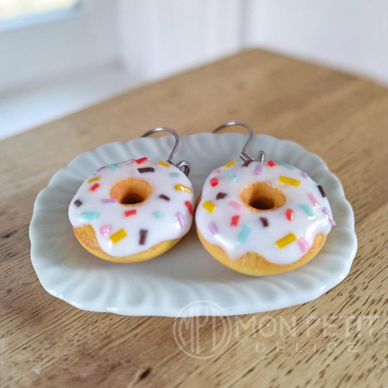 Angled view of the white donut earrings showing the golden dough base and glaze.
