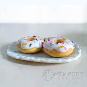 Macro close-up of the glossy white icing and rainbow sprinkles on foodie jewelry.