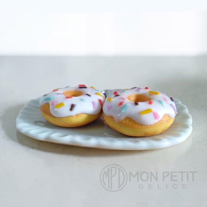 Macro close-up of the glossy white icing and rainbow sprinkles on foodie jewelry.
