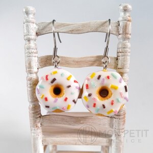 Polymer clay white donut earrings displayed on a rustic miniature wooden chair.