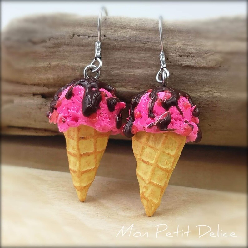 May include: A pair of pink and brown ice cream cone earrings with chocolate sauce and sprinkles. The earrings are made of polymer clay and have silver hooks.