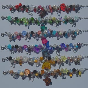 May include: Six charm bracelets arranged in a vertical row, each featuring a silver-tone chain adorned with a variety of colorful beads, including translucent, opaque, and metallic spheres, stars, hearts, music notes, and unique character charms.