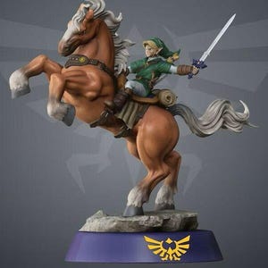 Op de afbeelding: Een beeldje van Link uit The Legend of Zelda, rijdend op Epona, een bruin paard met een witte manen en staart. Link draagt groene kleding en houdt een zwaard vast. Het beeldje staat op een blauwe basis met een gouden Triforce-symbool.
