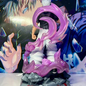 May include: A detailed figurine of a character with white hair and a black shirt, standing in a dynamic pose with purple energy effects. The figurine is set on a base with a gray, rocky texture and red splatters.