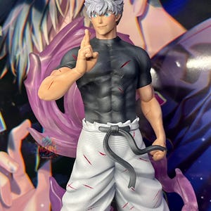 May include: A white and grey figure with spiky white hair, wearing a black shirt and white pants with a black belt. The figure has a serious expression and is holding up one finger. The figure is standing in front of a purple and blue background.