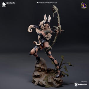 May include: A black and white 3D printed figurine of a female archer with bunny ears, holding a bow and arrow. The figurine is standing on a rocky base with green plants.