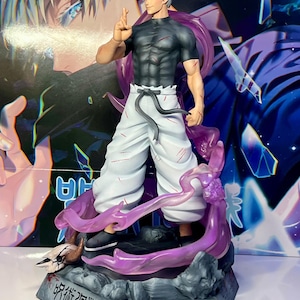 May include: A white and black anime figurine of a character with white hair and a black shirt. The figurine is standing on a gray base with purple smoke effects. The base has the text "呪術廻戦" in Japanese.