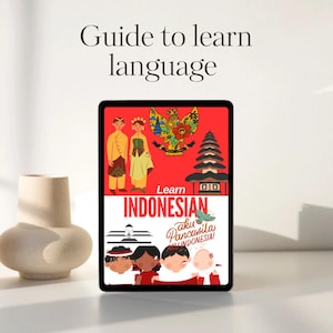 Pode incluir: Um tablet digital exibe um gráfico vermelho e branco com o texto "Learn Indonesian". A imagem inclui ilustrações de figuras tradicionais indonésias, um templo e o texto "Guide to learn language."