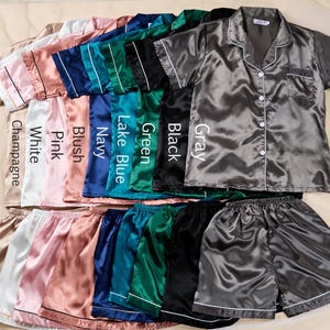 K&ouml;nnte beinhalten: Satin-Pyjama-Sets in verschiedenen Farben: Champagner, Wei&szlig;, Rosa, Rouge, Marineblau, Seeblau, Gr&uuml;n, Schwarz und Grau. Jedes Set besteht aus einem kurz&auml;rmeligen Hemd mit Kn&ouml;pfen und passenden Shorts, mit wei&szlig;er Paspelierung.