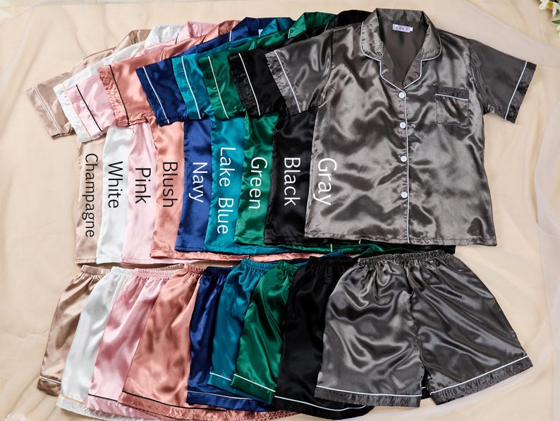 K&ouml;nnte beinhalten: Satin-Pyjama-Sets in verschiedenen Farben: Champagner, Wei&szlig;, Rosa, Rouge, Marineblau, Seeblau, Gr&uuml;n, Schwarz und Grau. Jedes Set besteht aus einem kurz&auml;rmeligen Hemd mit Kn&ouml;pfen und passenden Shorts, mit wei&szlig;er Paspelierung.